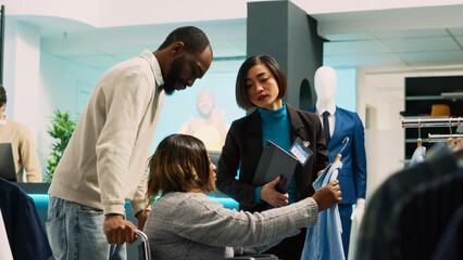 Obraz premium Female client with disability coming to buy clothes, looking to increase wardrobe in clothing store. Young woman wheelchair user shopping for modern trendy wear, market boutique. Handheld shot.