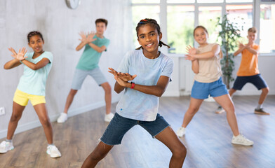 Fototapeta premium Smiling african american preteen boy dancer practicing active vigorous dance with group in modern studio..