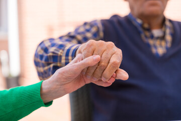 Detail of the hands of two elderly people in the garden of a nursing home or retirement home holding hands in a moment of affection
