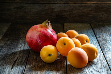 Naklejka na ściany i meble Ripe whole pomegranates and apricots on a wooden table.