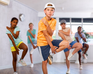 Fototapeta premium Dynamic little boy training Break-dance poses in dancehall with other attendees of dancing courses