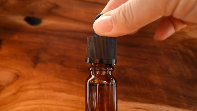 A bottle of cosmetic oil for skin care in the wooden background. Holds a pipette with medicinal oil. Alternative medicine, vitamins C and squalene, cosmetic serum, hyaluronic acid. Dark brown glass.