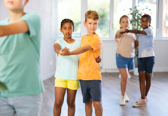 Cheerful preteen boy and girl training movements of slow foxtrot in dance studio with multiethnic...