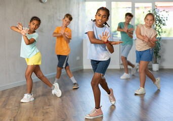 Fototapeta premium African man child dances waacking in choreographic school, group of young people in sportswear trains together with their classmates in gym before competitions, battle