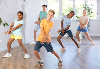 Group of positive juvenile boys and girls engaged in Breakdancing in training room during workout session