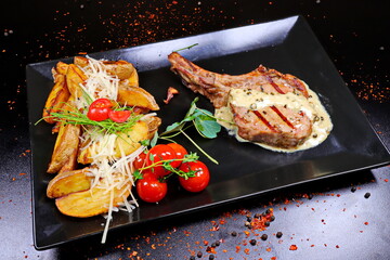 Roasted lamb chops with potatoes and sauce on black plate in restaurant - 619607416
