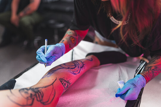 Freehand technique concept, tattoo artist drawing on a leg with a blue marker. High quality photo