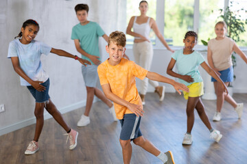 Cheerful tween boy practicing energetic dance movements with group of children in choreography...