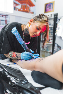 Caucasian tattoo master girl working with a tattoo machine in the studio, medium vertical shot. High quality photo