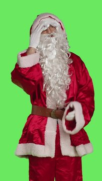 Vertical video Front view of father christmas with painful headache standing in studio over greenscreen backdrop, unwell man in saint nick red suit. Sick festive character with migraine feeling hurt