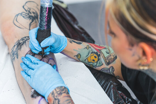 girl tattooist drawing a tattoo on a customer's leg, working in the art studio. High quality photo