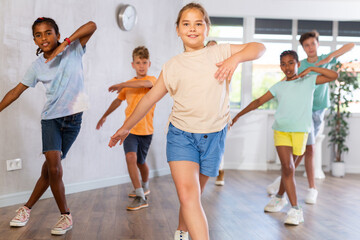 Positive girl dances hip hop in choreographic school, group of young people in sportswear trains...