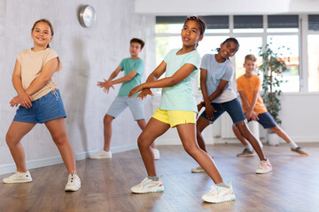 Fototapeta premium Portrait of cheerful preteen african american girl enjoying active dancing during group training in dance studio..