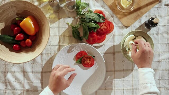 Caprese salad preparation. Top view image of man's hands mixing slices of tomato, cheese and basil on plate. Concept of hobby, culinary, food preparation, taste, diet, healthy dish, ad