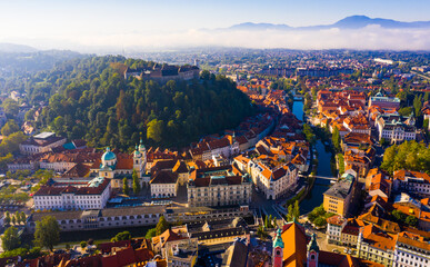 Fototapeta premium Aerial view of Slovenian town of Ljubljana overlooking fortified castle on hill and Roman Catholic Cathedral in morning sunlight