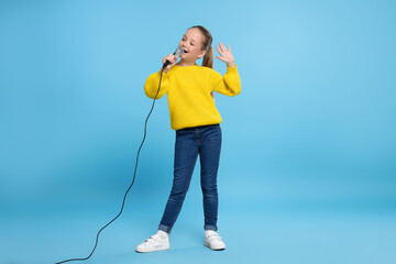 Cute little girl with microphone singing on light blue background