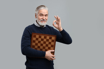 Man with chessboard showing OK gesture on light gray background. Space for text