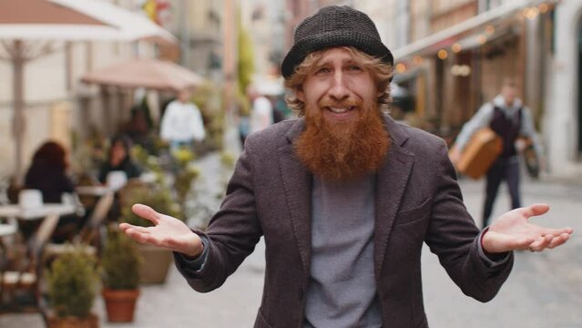 What. Why. Surprised frustrated young bearded man raising hands asking reason of failure, demonstrating disbelief irritation by troubles outdoors. Confused redhead guy walking in urban city street