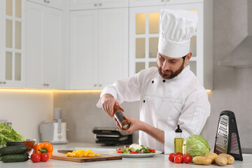 Professional chef adding pepper into delicious salad at marble table in kitchen