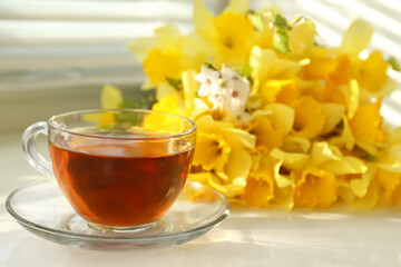 Cup of aromatic tea and beautiful yellow daffodils on windowsill