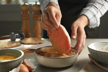 Woman cooking schnitzel at grey table indoors, closeup