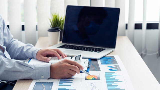 Young financial market analyst working at office with laptop while sitting at wooden table Businessman analyzing documents on his desk close up pictures