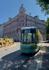 Famous green tram moving through beautiful streets of Helsinki with ornate pink and white building in the background.