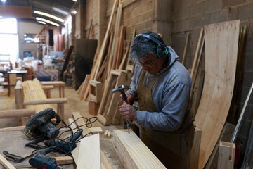 Mastering the Trade: Experienced Artisan Employing Hammer and Chisel on Woodwork in a Woodworking Studio