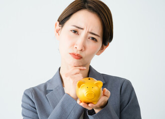 豚の貯金箱を持って悩む若い女性　ビジネスイメージ	
