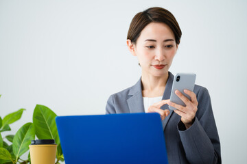 ノートパソコンとスマートフォンを使う若い女性　ビジネスイメージ	
