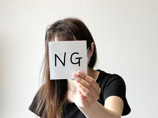 顔の前でNGの文字入り紙を片手で持つ女性