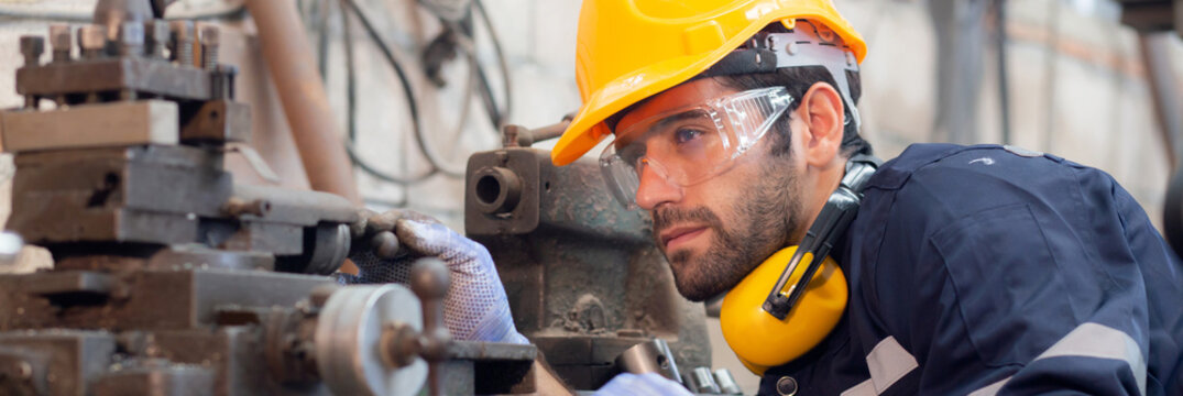 Young caucasian engineer man operating lathe machine for preparing production at factory industrial, technician or labor maintenance machinery at workplace, metalworker working, industry concept.