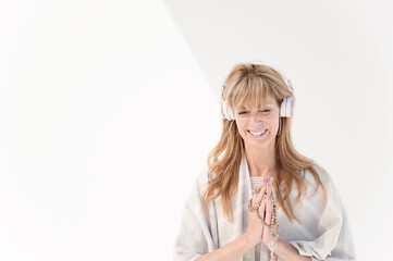 Photograph of a spiritual middle aged woman on a white background using headphones.  - 619636854