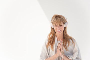 Photograph of a spiritual middle aged woman on a white background using headphones.  - 619636865