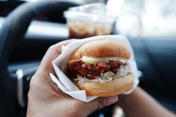 Asian woman driver hold and eat hamburger in car, dangerous and risk an accident.