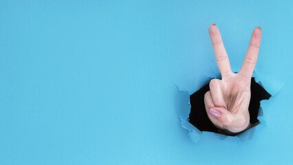 Peace gesture. Victory sign. Female hand showing number two with fingers inside breakthrough paper...