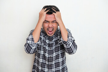 Adult Asian man screaming and grabbing his hair showing stress expression