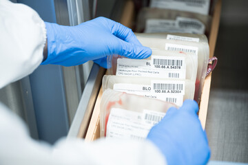 Close up scientist hand holding red blood bag in storage refrigerator at blood bank unit...