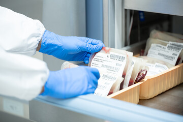 Close up scientist hand holding red blood bag in storage refrigerator at blood bank unit laboratory.Blood bags received from blood donations will be used in patient.Save life medical concept. - obrazy, fototapety, plakaty