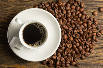cup of black coffee on wood and roasted coffee beans and two sugar cubes. top view
