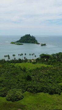 Aerial view of tropical island with green trees under clear sky and clouds. Davao Oriental, Philippines. Vertical view. Seascape.