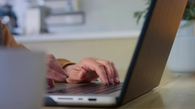 The old man is working on a laptop. A pensioner types with his fingers on a computer keyboard. An old man has a freelance job outside the house. Modern work for seniors. Close up