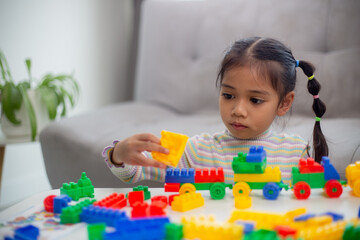 Adorable little girl playing toy blocks in a bright room.