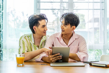 Attractive male lgbtq collegues working together with using digital tablet and paper showing graphic chart in living room, Lgbt love concept