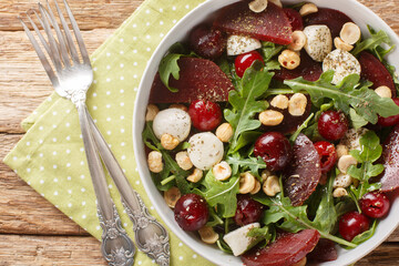Fototapeta na wymiar Vegetarian salad of arugula, beets, ripe cherries, cheese, hazelnuts close-up in a bowl on the table. Horizontal top view from above