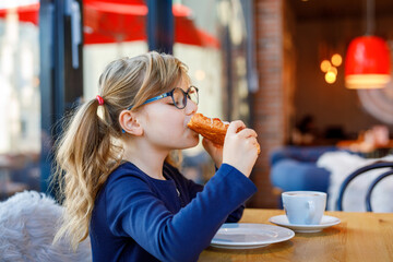 Adorable smiling girl with glasses have a breakfast in a cafe. Preschool child with glasses...
