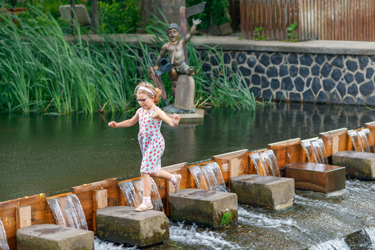 Cute little preschool girl having fun by a river on warm and sunny summer day. Happy excited preschool child running on stones.
