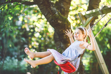 Happy little preschool girl having fun on swing in domestic garden. Cute healthy child swinging...