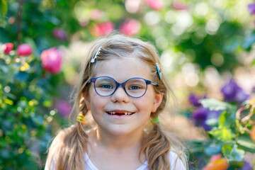 Portrait of a cute preschool girl with eye glasses and big teeth gap outdoors in park. Happy funny child on sunny summer day. Kid loosing milk tooth