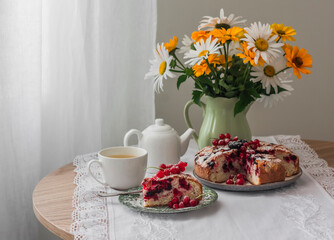 Summer tea party - a cup of green tea, berry pie, a jug of daisies on a round table in a cozy...